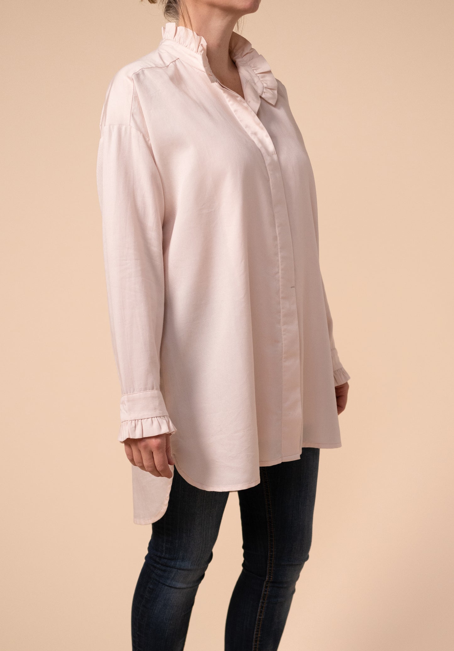 Front and side view of Effin's breastfeeding friendly light pink blouse showing the ruffles on the neck and cuffs. The top two buttons on the neck are undone.