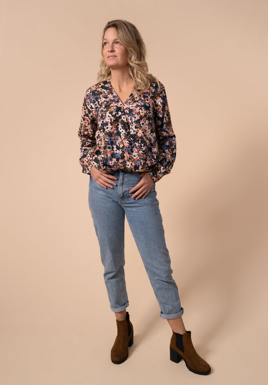 image shows Effin's floral breastfeeding friendly wrap blouse tucked into a pair of mom jeans, paired with brown boots. The floral print is on a orange ground and the flowers are blue, yellow, green, and navy. They small in size.